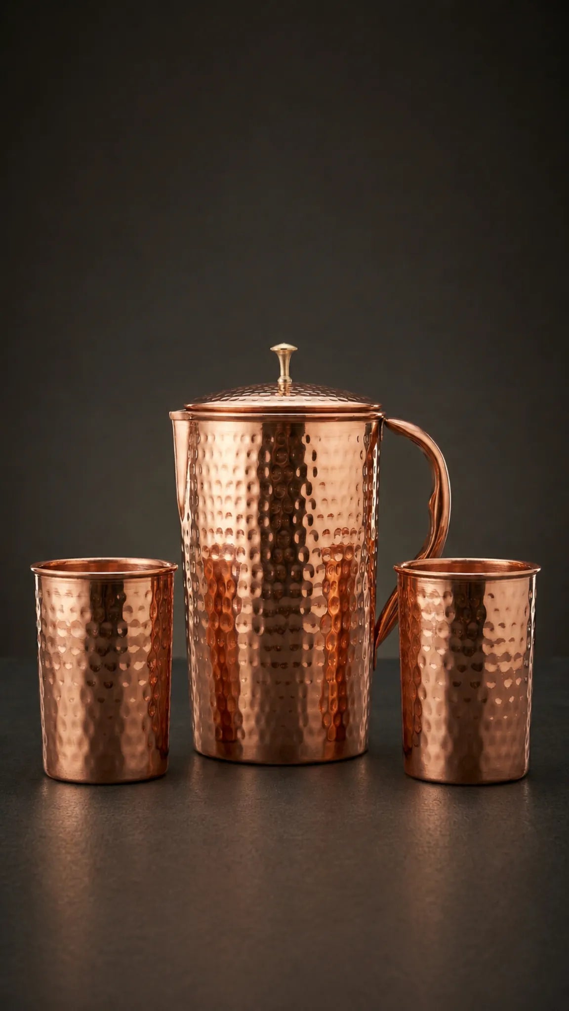 Copper pitcher and two cups on a dark background