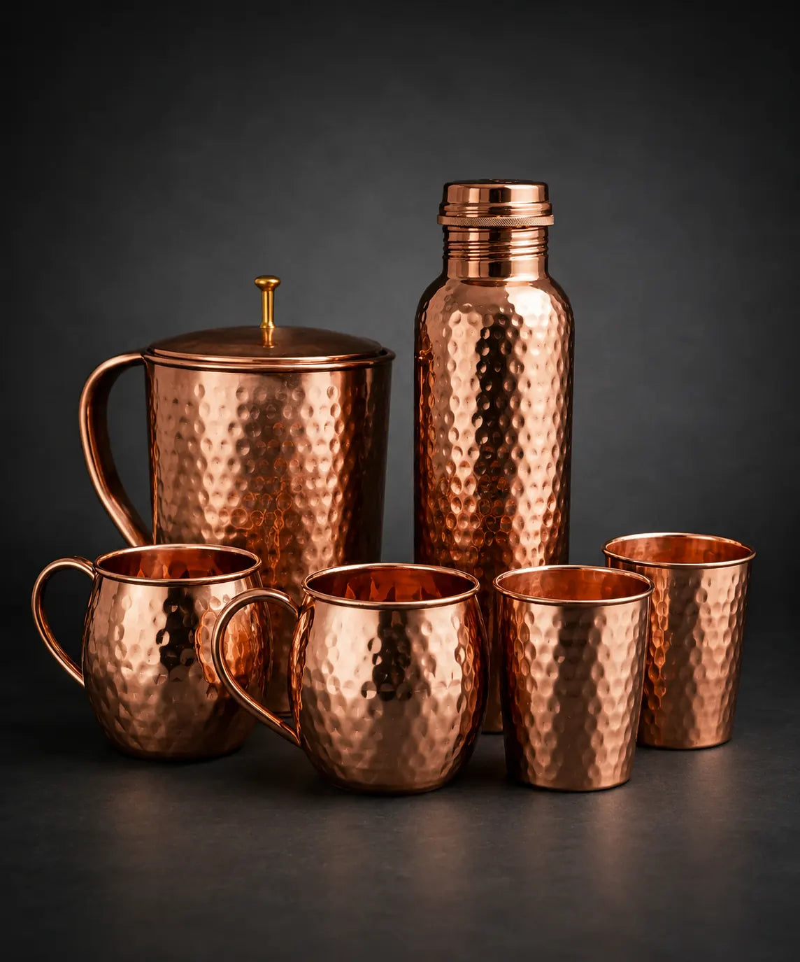 Set of copper kitchenware including mugs and a bottle on a dark background